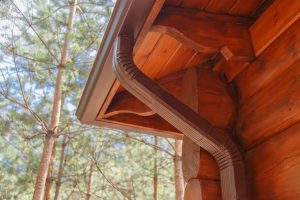 Roof seamless gutter system on log house in a forest.